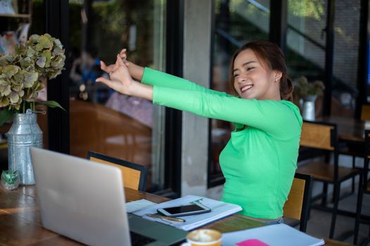 Asian woman stretching after reading book and work hard and smiling in coffee shop