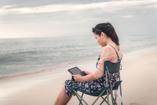 Freelancer Woman is Working on Tablet While Travel Vacation Trip at The Beach, Smart Woman is Using Tablet for Communication and Entertainment at Outdoor Sand Beach. Freelance and Relaxation Concept.