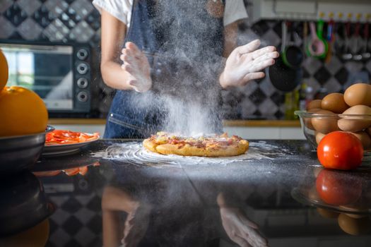 Asian women preparing a pizza, knead the dough and puts ingredients on kitchen table