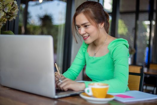 Asian businesswomen smiling and using notebook for analysis documents and graph financial diagram working and she is drinking coffee at coffee shop