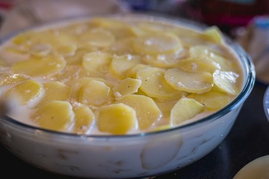 preparation of a gratin dauphinois with its potatoes, its cream and its condiments in a pan on the worktop of a kitchen