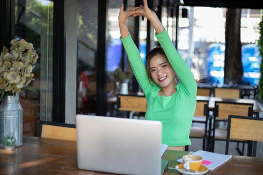 Asian woman stretching after reading book and work hard and smiling in coffee shop