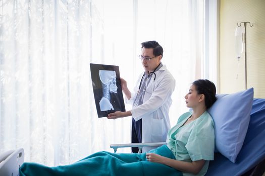 The doctor is explaining about the brain X-ray results to a female patient lying in bed at a hospital