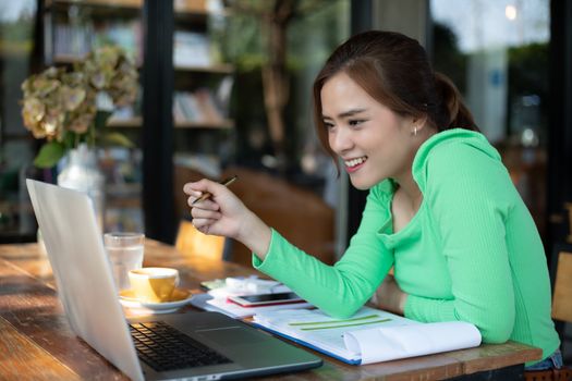 Asian businesswomen smiling and using notebook for analysis documents and graph financial diagram working and she is drinking coffee at coffee shop