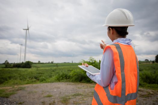 Asian engineer with hardhat using  tablet pc computer inspecting and working at wind turbine farm Power Generator Station
