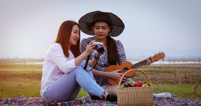 A group of Asian friends playing Ukelele and spending time making a picnic in the summer holidays.They are happy and have fun on holidays. They using notebook for working