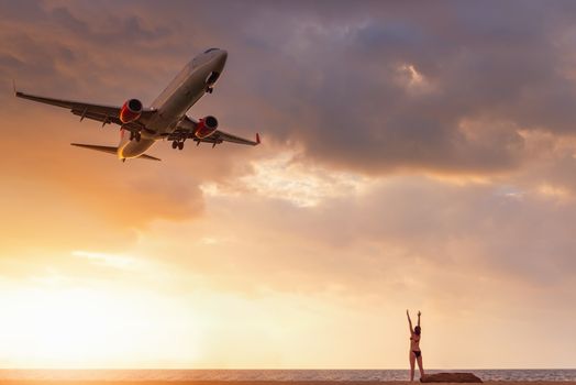 Travel Destination and Vacation in Summer, Sexy Woman Having Fun While Capturing Photos Airplane is Flying Over The Beach. Tourist Woman Relaxing on Tropical Beach and Enjoy Seeing Landing Aircraft.