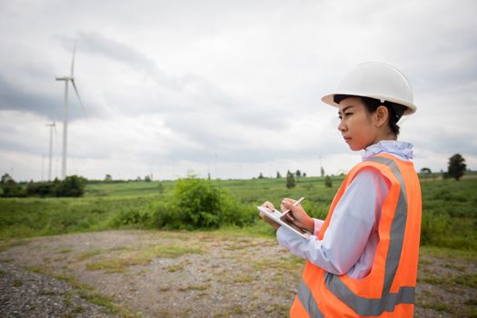 Asian engineer with hardhat using  tablet pc computer inspecting and working at wind turbine farm Power Generator Station