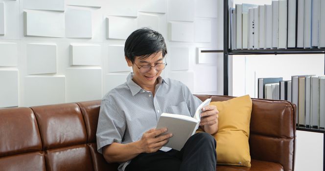 Senior Asian man reading book on sofa in living room at home ,Portrait of Asian elderly man is Relaxing and Happiness With Read a Magazine