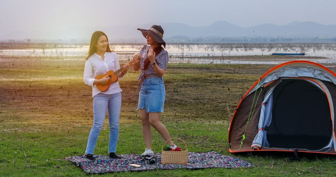 A group of Asian friends playing Ukelele and spending time making a picnic in the summer holidays.They are happy and have fun on holidays. They using notebook for working