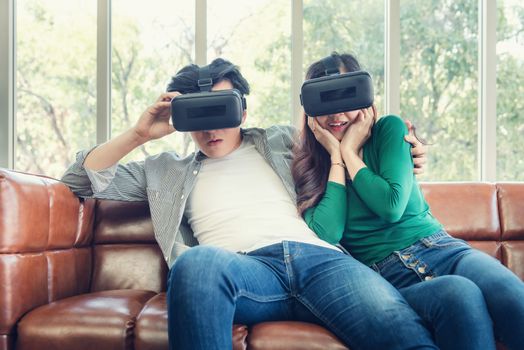 Young Couple Having Fun While Watching Video Via Virtual Reality Together. Couple Love Having Enjoyment With Electronic VR Goggles Gaming on Couch. Entertainment Innovation/Lifestyles Concept