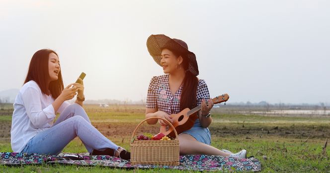A group of Asian friends playing Ukelele and spending time making a picnic in the summer holidays.They are happy and selfie ,Relax time on holiday concept travel