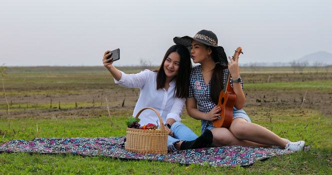 A group of Asian friends playing Ukelele and spending time making a picnic in the summer holidays.They are happy and selfie ,Relax time on holiday concept travel