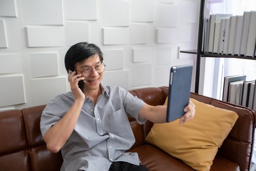 Senior Asian man playing tablet and video call on sofa in living room at home  Portrait of Asian elderly man is Relaxing and Happiness With playing tablet