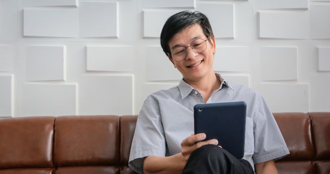 Senior Asian man playing tablet and video call on sofa in living room at home  Portrait of Asian elderly man is Relaxing and Happiness With playing tablet