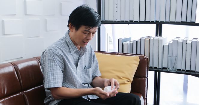 Asian senior man taking medicine on sofa at home