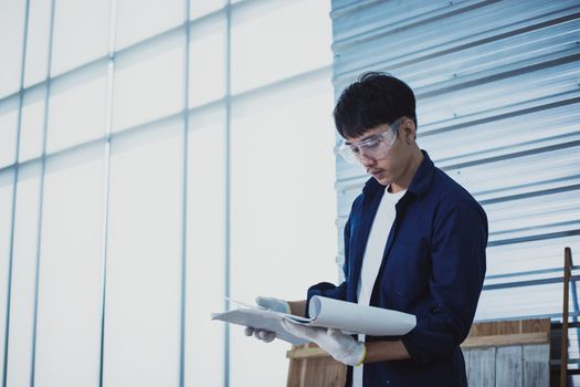 Asian man Carpenter working with technical drawing or blueprint construction paper lying on a workshop with carpentry tools and wood at home