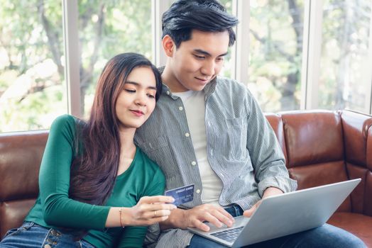 Young Couple Love Relax Enjoyment While Online Shopping on Electronic Laptop in Living Room, Portrait of Asian Couple Relaxing on a Couch During Shopping Online Togetherness. Relaxation/ Lifestyle