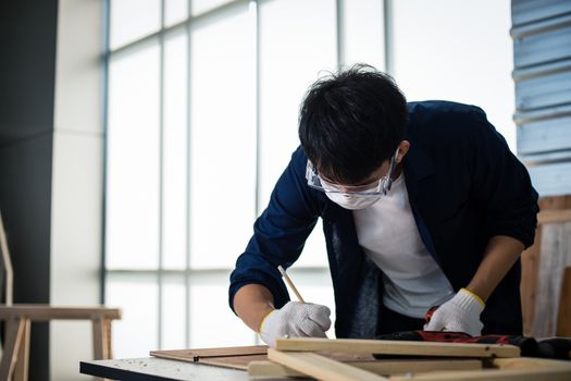 Asian man Carpenter working with technical drawing or blueprint construction paper lying on a workshop with carpentry tools and wood at home