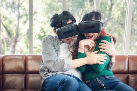 Young Couple Having Fun Exciting While Watching Video Via Virtual Reality Together. Couple Love Enjoying With Electronic VR Video Gaming on The Couch. Entertainment Innovation/Virtual Reality Concept
