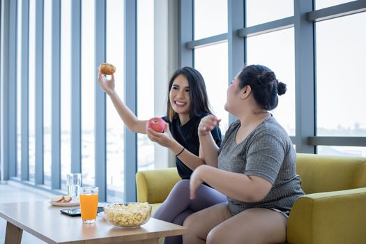 Overweight woman and asian girl enjoy eating food on sofa at home