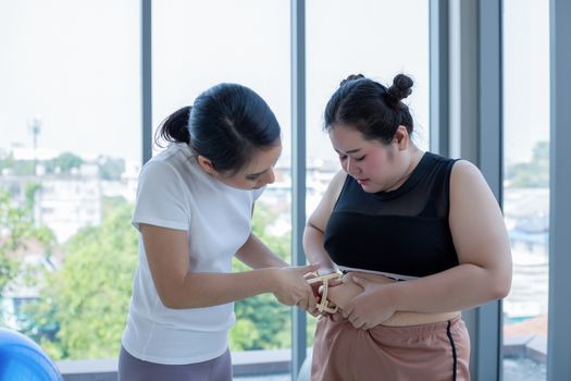 Young female trainer measuring fat layer of overweight woman with caliper at fitness