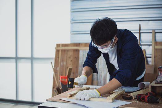 Asian man Carpenter working with technical drawing or blueprint construction paper lying on a workshop with carpentry tools and wood at home