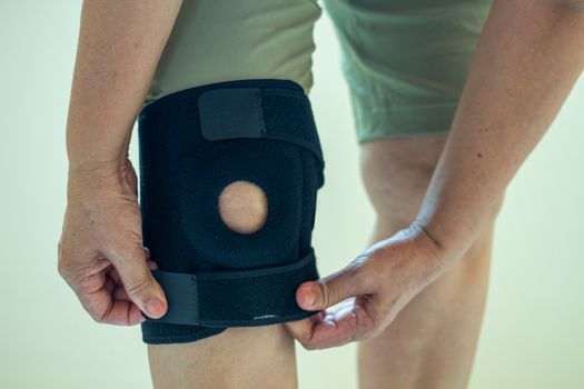 old Asian women to knee injury and use knee support brace on leg 