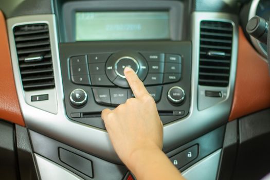 Asian Women press button on car radio for listening to music.