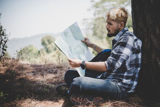 Hiker relaxing by tree looking at map, go adventure in mountain.