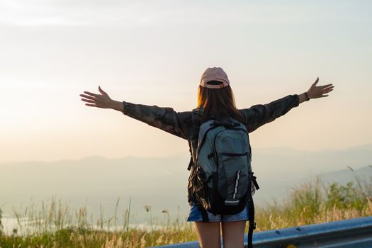 Freedom traveler woman standing with raised arms and enjoying a beautiful nature and cheering young woman backpacker at sunrise seaside mountain peak