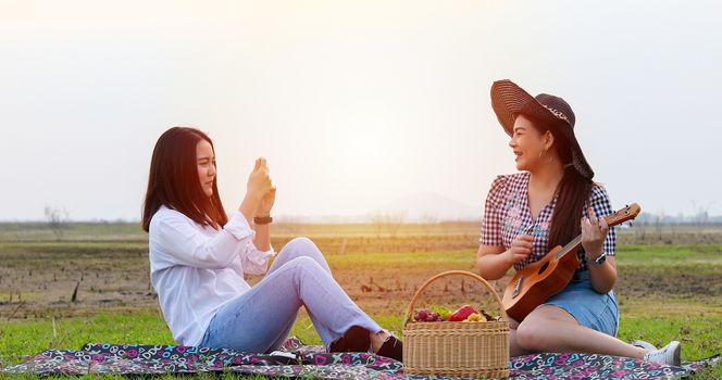 A group of Asian friends playing Ukelele and spending time making a picnic in the summer holidays.They are happy and selfie ,Relax time on holiday concept travel