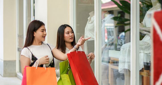 Asian women with friend are holding shopping bags and using a smart phone and smiling while doing shopping in the supermarket/mall