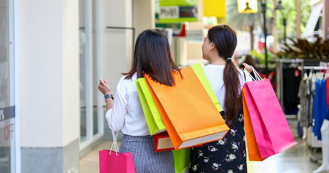 Asian women with friend are holding shopping bags and using a smart phone and smiling while doing shopping in the supermarket/mall