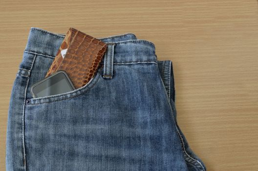 leather wallet and smart phone in jeans pocket on wooden background