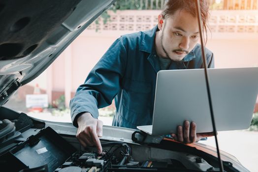 Mechanic Engineer is Diagnosing Car Engine and Electric Adjusting Transmission With Computer Laptop, Automobile Service Man Diagnostic Vehicle Car Engines Systems in Garage Workshop. Engineering Work