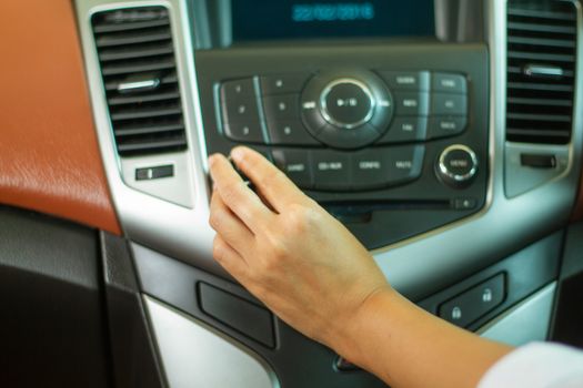 Asian Women press button on car radio for listening to music.