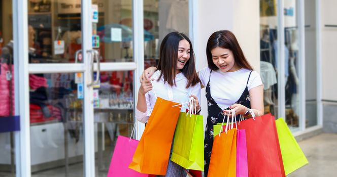 Asian women with friend are holding shopping bags and using a smart phone and smiling while doing shopping in the supermarket/mall