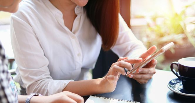 Two Asian women drinking coffee in a cafe and shopping online on smart phones