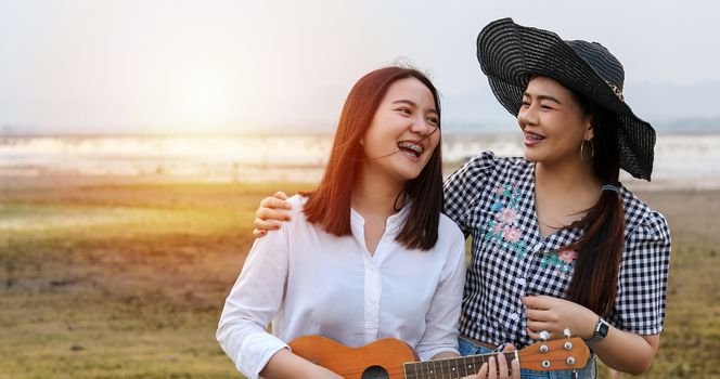 A group of Asian friends playing Ukelele and spending time making a picnic in the summer holidays.They are happy and have fun on holidays.