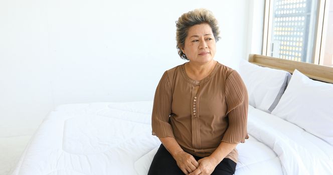 An elderly woman sitting alone on the bed