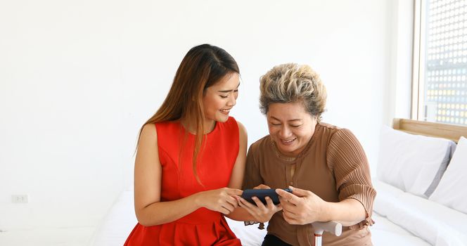 Cheerful young girl with an elderly woman playing together with digital tablet at home