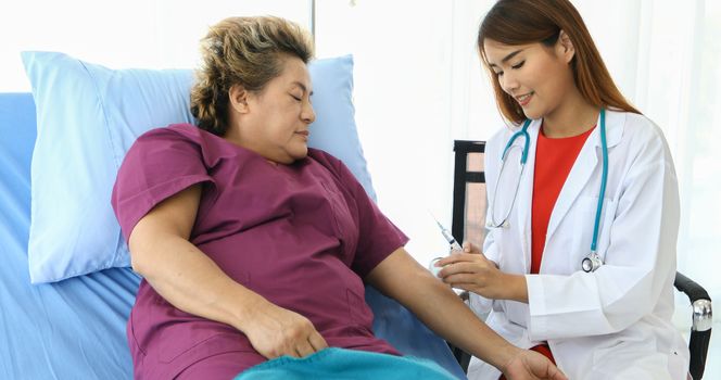 The doctor is using the syringe for the old woman lying in bed