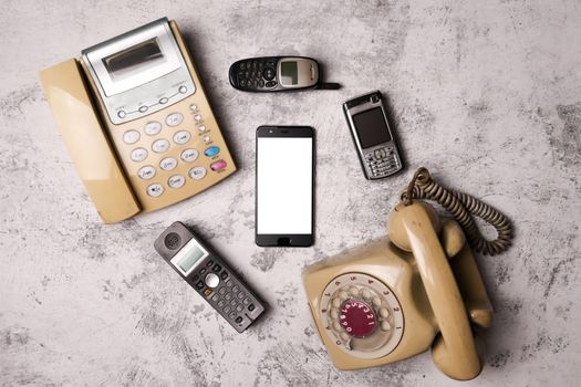 An old telephone with rotary dial, a landline, an obsoleted cellphone and smartphone on a grunge background.