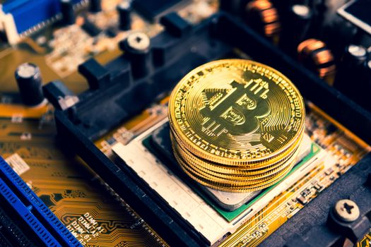 Stack of golden coins with bitcoin symbol on a mainboard.