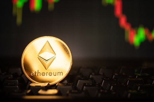 A golden coin with ethereum symbol on computer keyboard with stock graph background.