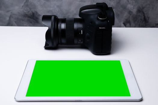 A black digital camera and a blank screen tablet on a table.