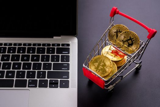 Golden coins with bitcoin symbol in a little shopping cart and a computer.
