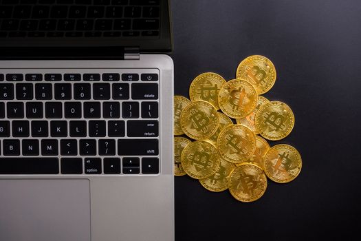 Computer and golden coins with bitcoin symbol on a black background.