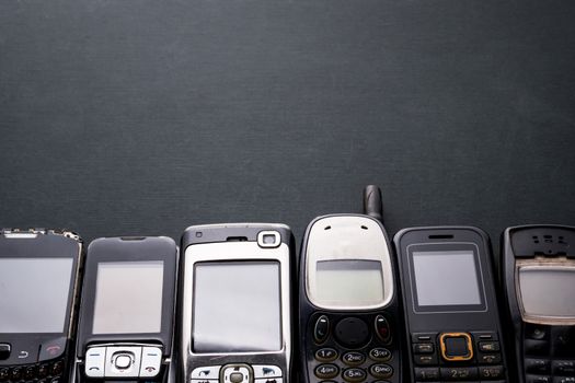 Old and obsoleted cellphones on a black background.
